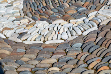 Oval pebbles or stones are laid in a pattern. White cobblestones are lined with a bend. The stones lie close to each other. Decoration for garden. The pebbles are illuminated by sunlight.