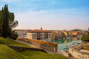 Fototapeta na wymiar High angle view of the canal of Peschiera del Garda, an ancient town on the shore of Lake Garda, with the typical colored houses and moored boats in a sunny spring day, Veneto, Italy