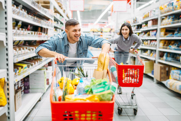 Young couple ride on trolleys in supermarket, 
