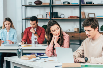 Multiethnic students sitting at desk and using laptop while studying in classroom