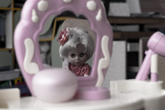 Female doll face with creepy eyes in the mirror. The reflection of the doll in the mirror
