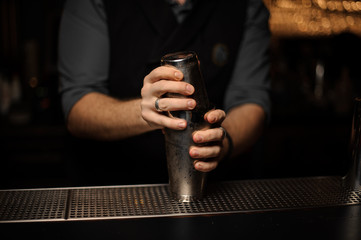 Professional bartender holding a steel shaker with a cocktail