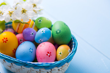 Fototapeta na wymiar Variety of decorated colorful Easter eggs in basket with white spring flowers on light blue background