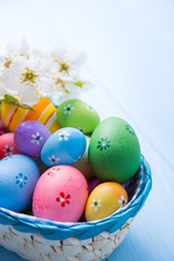 Fototapeta na wymiar Variety of decorated colorful Easter eggs in basket with white spring flowers on light blue background
