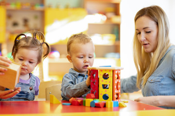 Kindergarten teacher playing with little kids in nursery. Developmental toys for preschool.