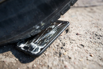 Broken and damaged smartphone with cracks on glass screen laying on ground. Accident. Cell phone under car wheel. Concept of warranty and lost smartphone 