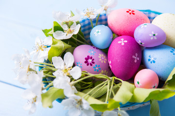 Obraz na płótnie Canvas Closeup set of decorated colorful Easter eggs in basket with white spring flowers on light blue background