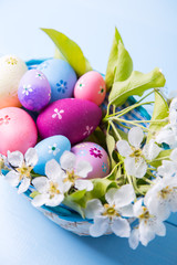 Closeup set of decorated colorful Easter eggs in basket with white spring flowers on light blue background