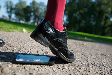 Woman step on the phone. Broken and damaged smartphone with cracks on glass screen laying on...