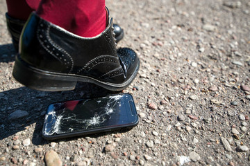 Woman step on the phone. Broken and damaged smartphone with cracks on glass screen laying on ground. Accident. Cell phone under shoe. Concept of warranty and lost smartphone 