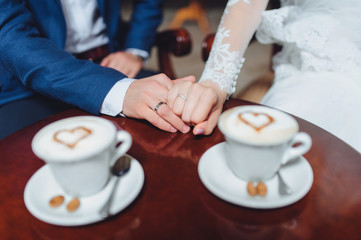 A newlywed couple is sitting in a beautiful cafe for a cup of coffee. White cups with cappuccino foam. Symbol of heart.