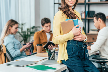 Cropped view of brunette student standing near table and holding books