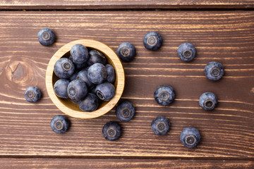 Lot of whole fresh sweet purple blueberry american with wooden bowl flatlay on brown wood