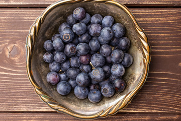 Lot of whole fresh sweet purple blueberry american in old iron bowl flatlay on brown wood