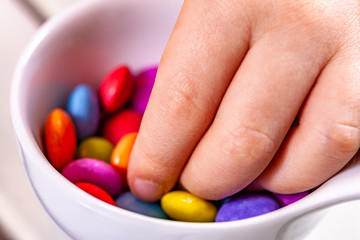 Child eating chocolate lentels from white bowl