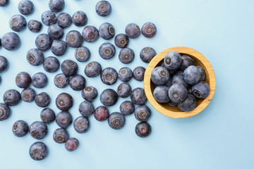 Lot of whole fresh sweet purple blueberry american with wooden bowl flatlay isolated on blue pastel background