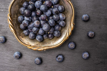 Lot of whole fresh sweet purple blueberry american in old iron bowl flatlay on grey stone