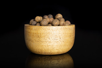Lot of whole dry brown allspice berries with wooden bowl isolated on black glass