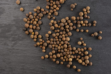 Lot of whole dry brown allspice berries flatlay on grey stone