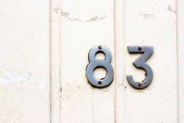 House number 83 with the eighty-three in silver metal lettering on a white planked wall