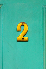 House number two with the 2 in golden bronze on a turquoise house door