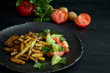 Freshly cooked fried potatoes with onions and mushrooms close-up on a plate. black wood table. horizontal view.