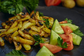 Freshly cooked fried potatoes with onions and mushrooms close-up on a plate. black wood table. horizontal view.