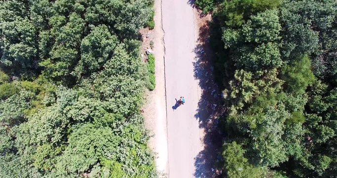 Aerial shot of a young attractive woman doing surf style turns on a skateboard on a road surrounded by mediterranean vegetation. 4k drone video forward and downward.