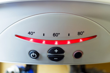 Close up of white electric tank-type storage water heater's control panel with black buttons and illuminated Celsius temperature indicator