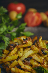 Freshly cooked fried potatoes with onions and mushrooms close-up on a plate. ebony table. vertical view of the dish.