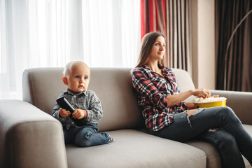 Mother watch tv, little male kid plays near