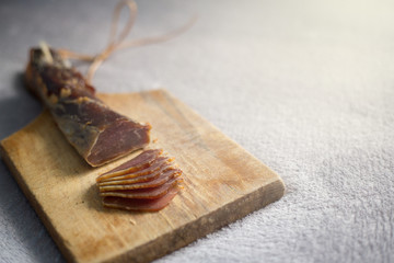 A dried ham on a wooden board cut into snacks.