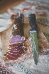 A dried ham on a wooden board cut into snacks with a knife next to it.