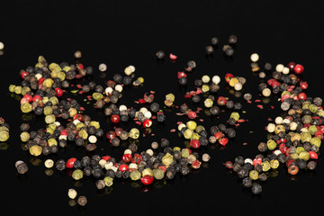 Lot of whole peppercorns of four colors isolated on black glass