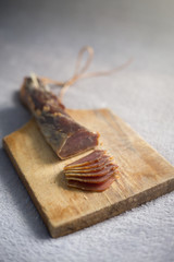 A dried ham on a wooden board cut into snacks.