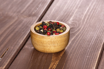 Lot of whole peppercorns of four colors with wooden bowl on brown wood