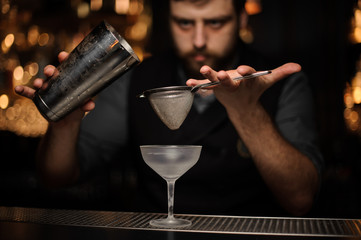 Professional bartender pouring cocktail from the shaker through the special sieve
