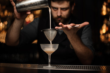 Bartender pouring cocktail from the shaker through the strainer