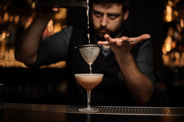 Brunette bartender pouring a creamy cocktail from the shaker through the strainer