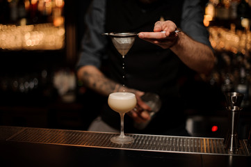 Professional bartender pouring a delicious cocktail through the sieve