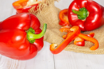 Group of two whole one half four slices of bulgarian red bell pepper on jute cloth on white wood