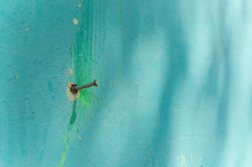 A nail on a green wall. Painting on the wall is peeling off. Selective focus.