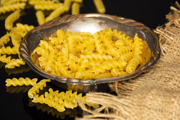 Lot of pieces of raw italitan yellow pasta torti on jute cloth in old iron bowl on black glass