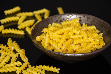 Lot of pieces of raw italitan yellow pasta torti in a grey ceramic bowl on black glass
