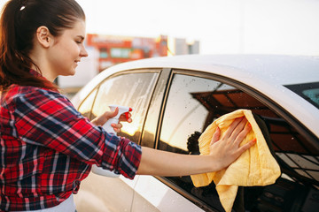 Woman cleans front glass of the car with spray