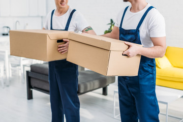 cropped view of two movers transporting cardboard boxes in apartment