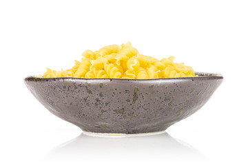 Lot of pieces of raw italitan yellow pasta torti in a grey ceramic bowl isolated on white background