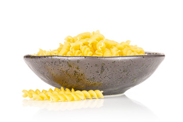 Lot of pieces of raw italitan yellow pasta torti in a grey ceramic bowl isolated on white background