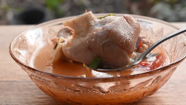 silver spoon scooping spicy boiled pork leg in Tom Yum soup on bowl