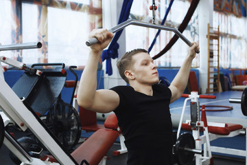 Young red-haired guy in a black t-shirt pumps muscles on a sports equipment.